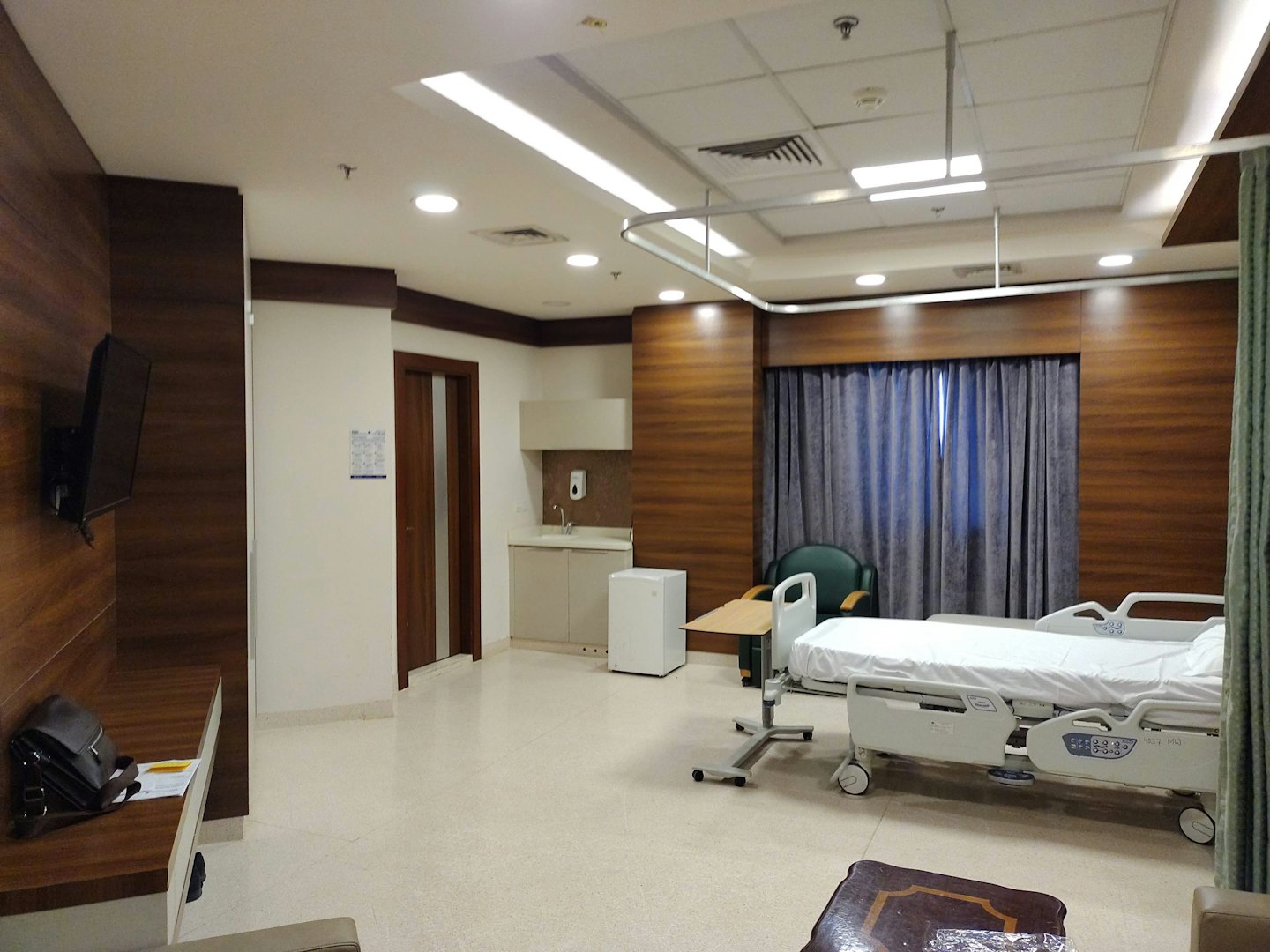 Ein modernes Krankenzimmer mit Bett, Sessel und Waschbecken.